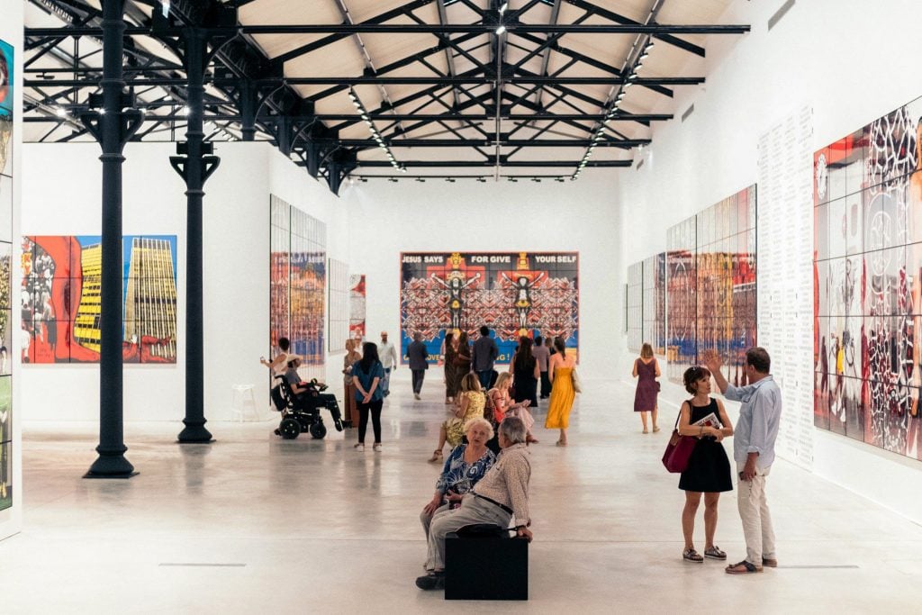 the interior of a vast museum with black rafters and the walls adorned with modern art 