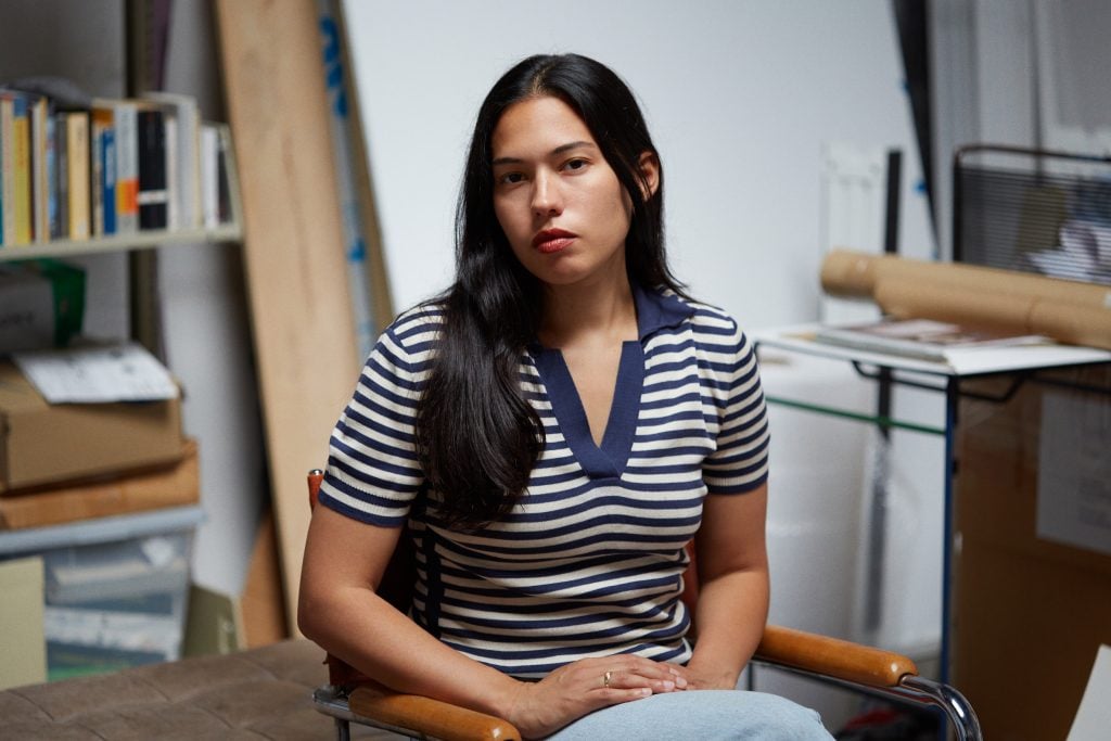 Portrait of the artist Rose Salane sitting with a navy striped v-neck tee shirt and her brown hair down.