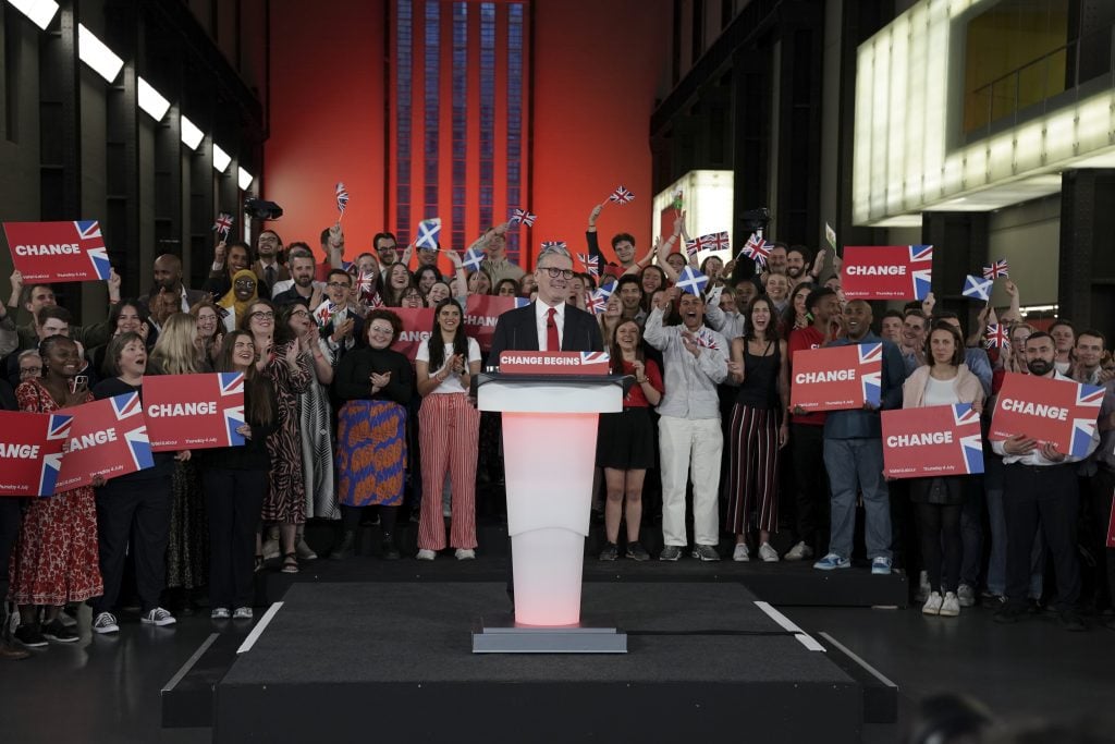 a man stands at a podium and his surrounded by a crowd holding signs