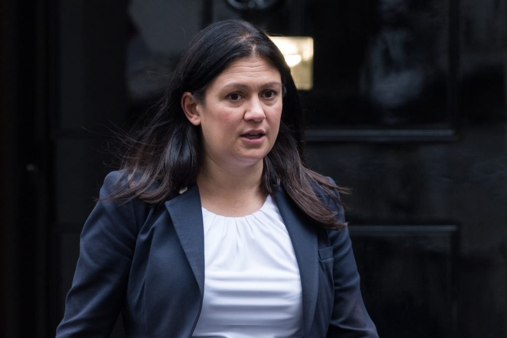 A woman with long, dark hair dressed in a dark grey blazer and white shirt