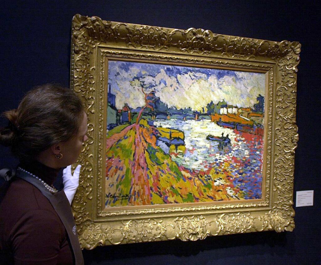 An art handler standing by a vivid landscape by Maurice de Vlaminck